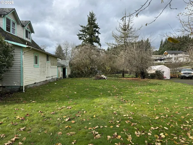 a view of a white house in front of a big yard with plants and large trees