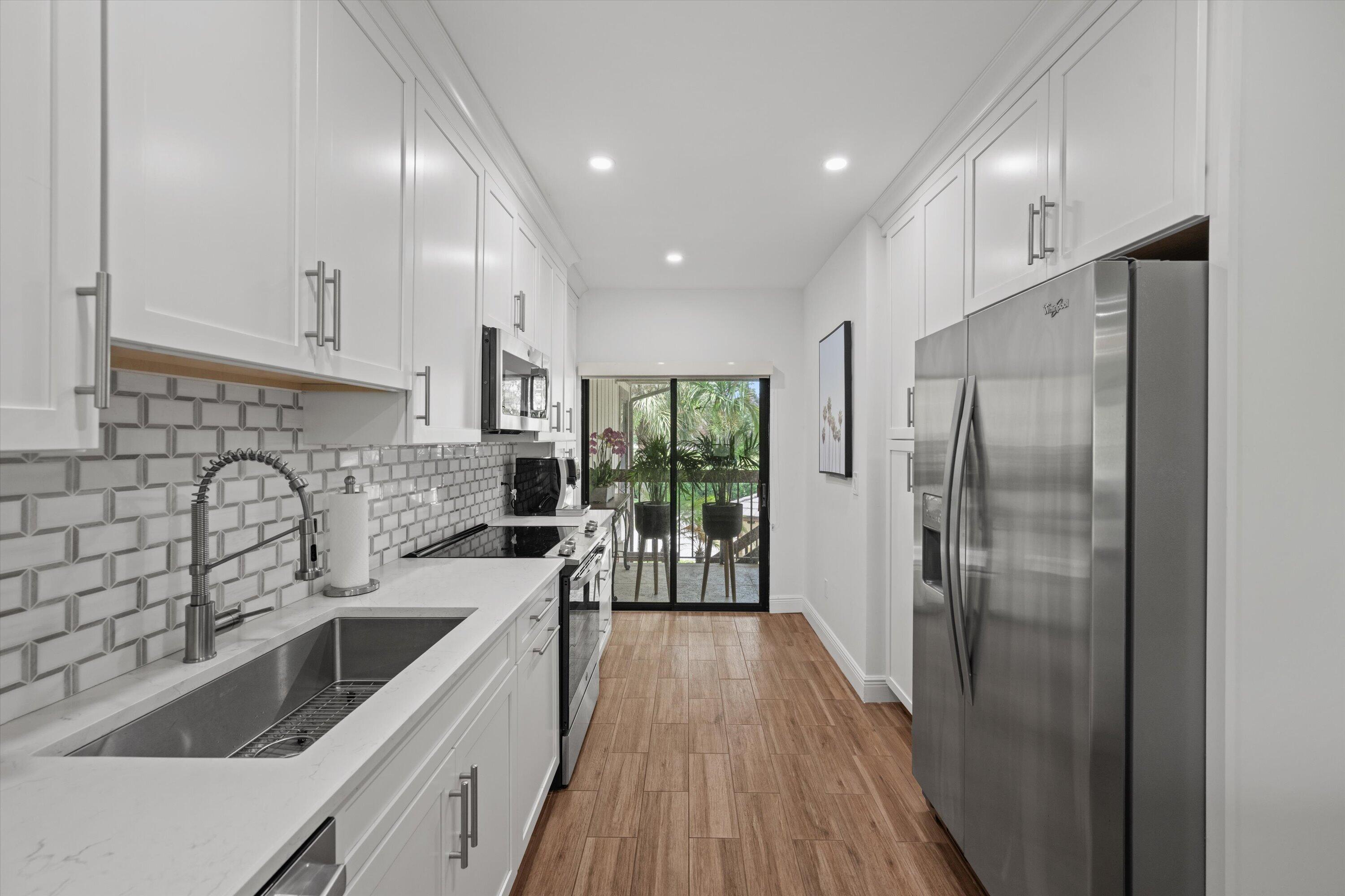 13400 Polo Road West, Unit 203 Wellington, FL 33414 - Photo 11 of 26 a kitchen with a refrigerator sink and white cabinets with wooden floor