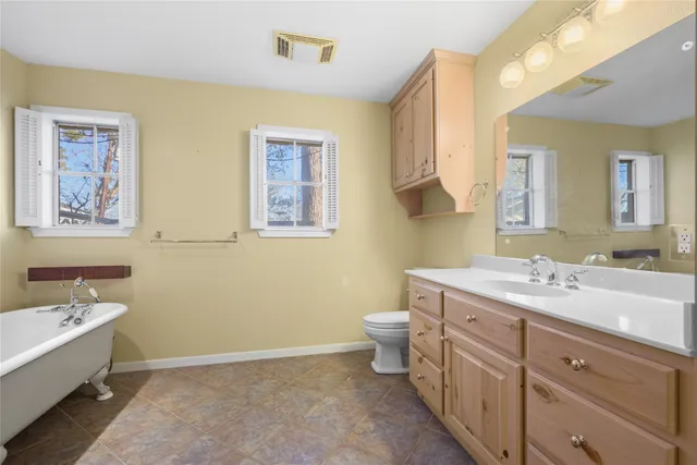 a spacious bathroom with a double vanity sink a large mirror a toilet and a bathtub