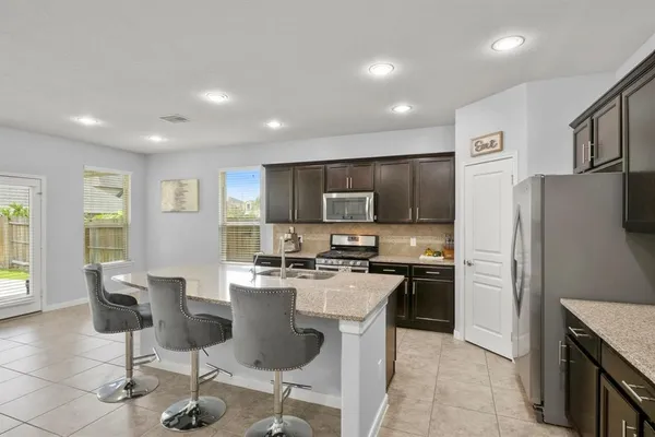 a kitchen with stainless steel appliances granite countertop a refrigerator a stove a sink a dining table and chairs