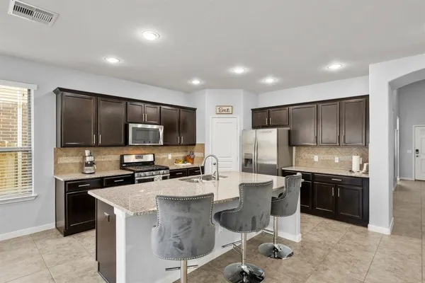 a kitchen with stainless steel appliances a stove top oven a sink a refrigerator and chairs