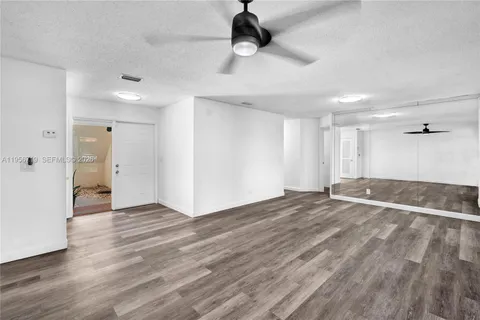 a view of an empty room with wooden floor and a ceiling fan