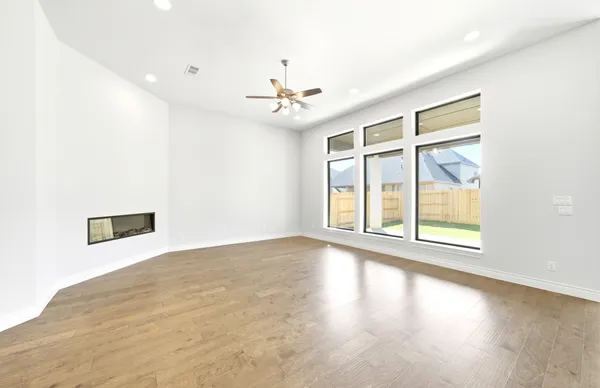 an empty room with wooden floor chandelier fan and windows