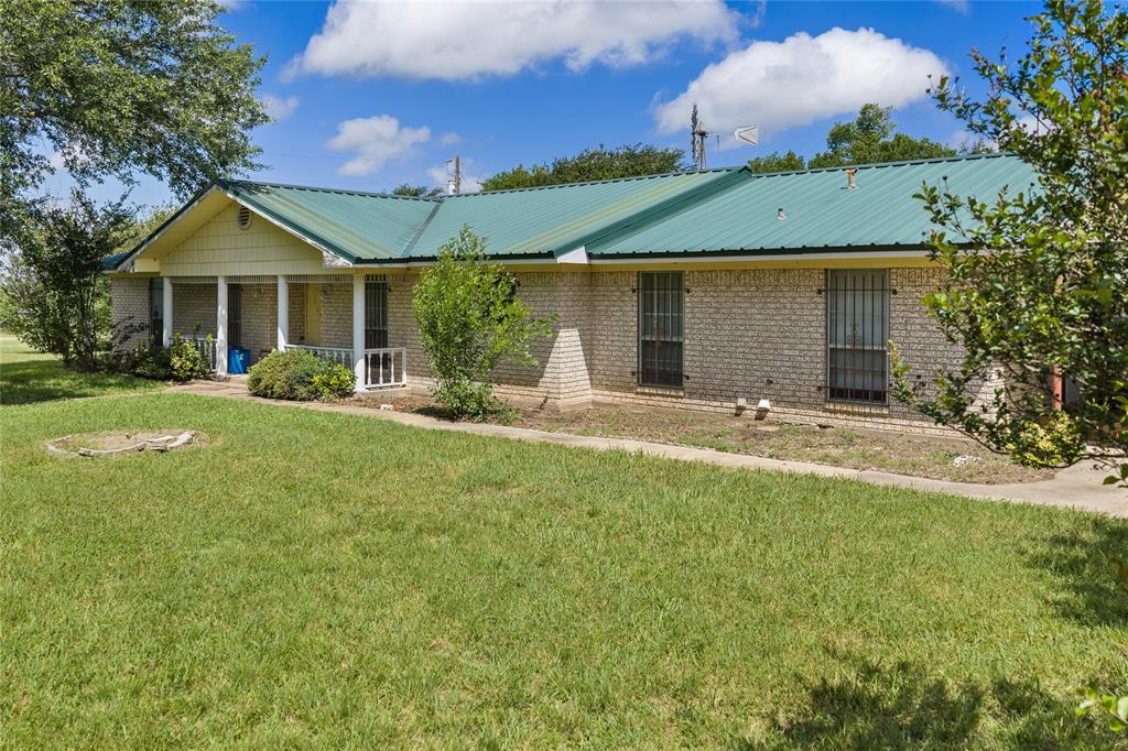 440 Williams Road Lorena, TX 76655 - Photo 15 of 19 Brick facade residence featuring a green metal roof, a covered front porch with white columns, and a landscaped front yard with mature trees