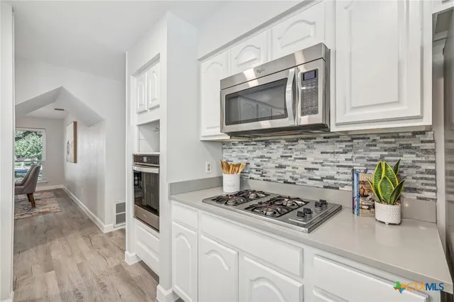 a kitchen with stainless steel appliances a stove a microwave a refrigerator a cabinets and wooden floor