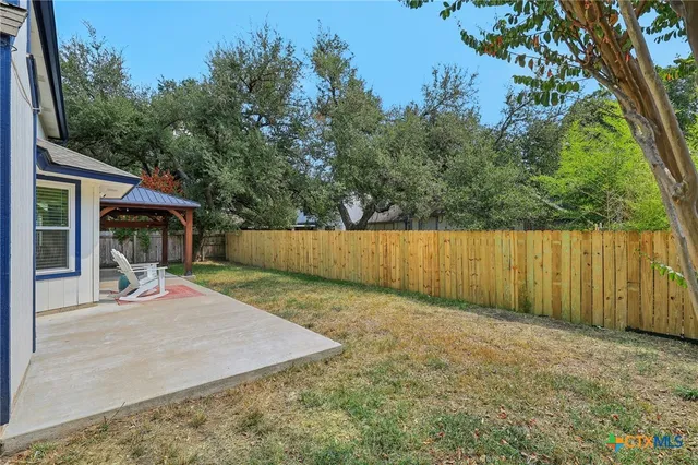a view of a backyard with large trees and wooden fence