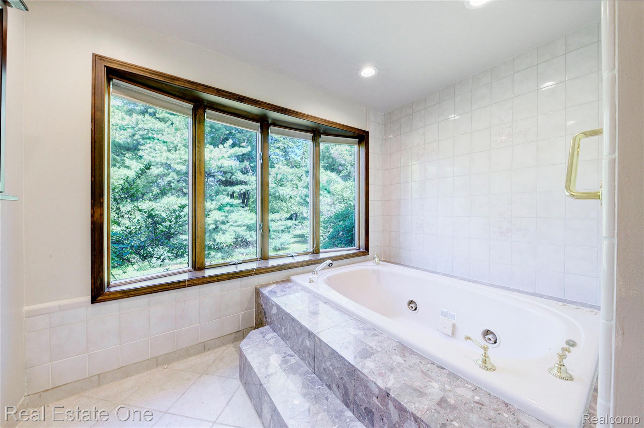 3125 West Commerce Road Milford, MI 48380 - Photo 30 of 63 Bay window featuring dark wood trim, an integrated jetted bathtub, a marble-finish surround with two-step entry, and white tile walls