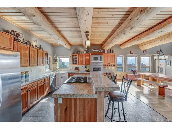 a kitchen with stainless steel appliances granite countertop a stove a refrigerator a kitchen island a dining table and chairs with wooden floor