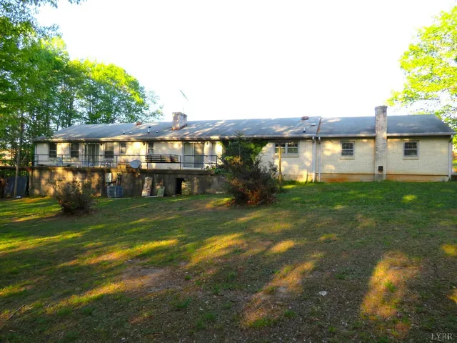 a view of a house next to a big yard with plants and large trees