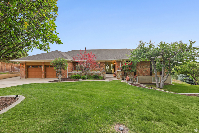 2342 Charros Road Sandy, UT 84092 - Photo 3 of 94 Brick facade residence featuring a two-car garage with wood-finish doors, a pitched shingle roof, and a green lawn