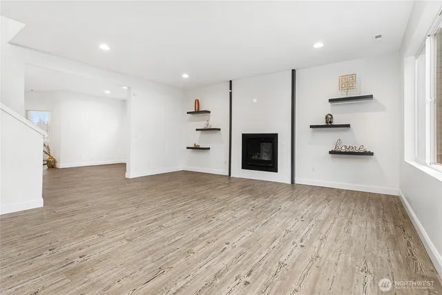a view of empty room with wooden floor and kitchen