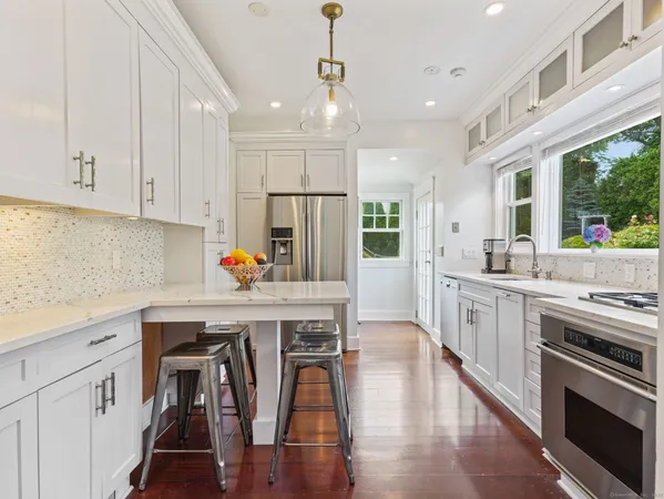 a kitchen with stainless steel appliances a stove a sink dishwasher a refrigerator white cabinets and wooden floor next to a window
