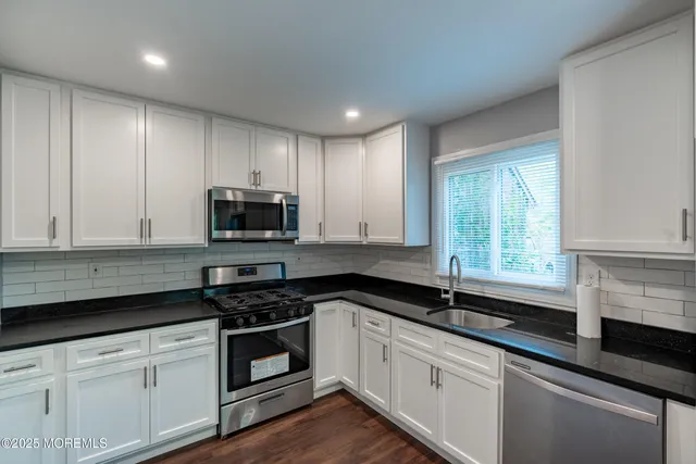 a kitchen with granite countertop white cabinets appliances a sink and a window