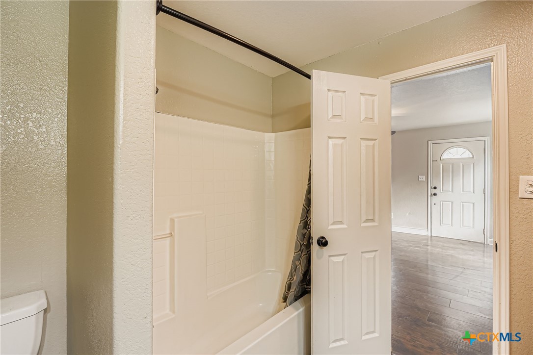 304 South Main Street Elgin, TX 78621 - Photo 22 of 25 Full bath featuring a textured wall, wood finished floors, and shower / bath combo