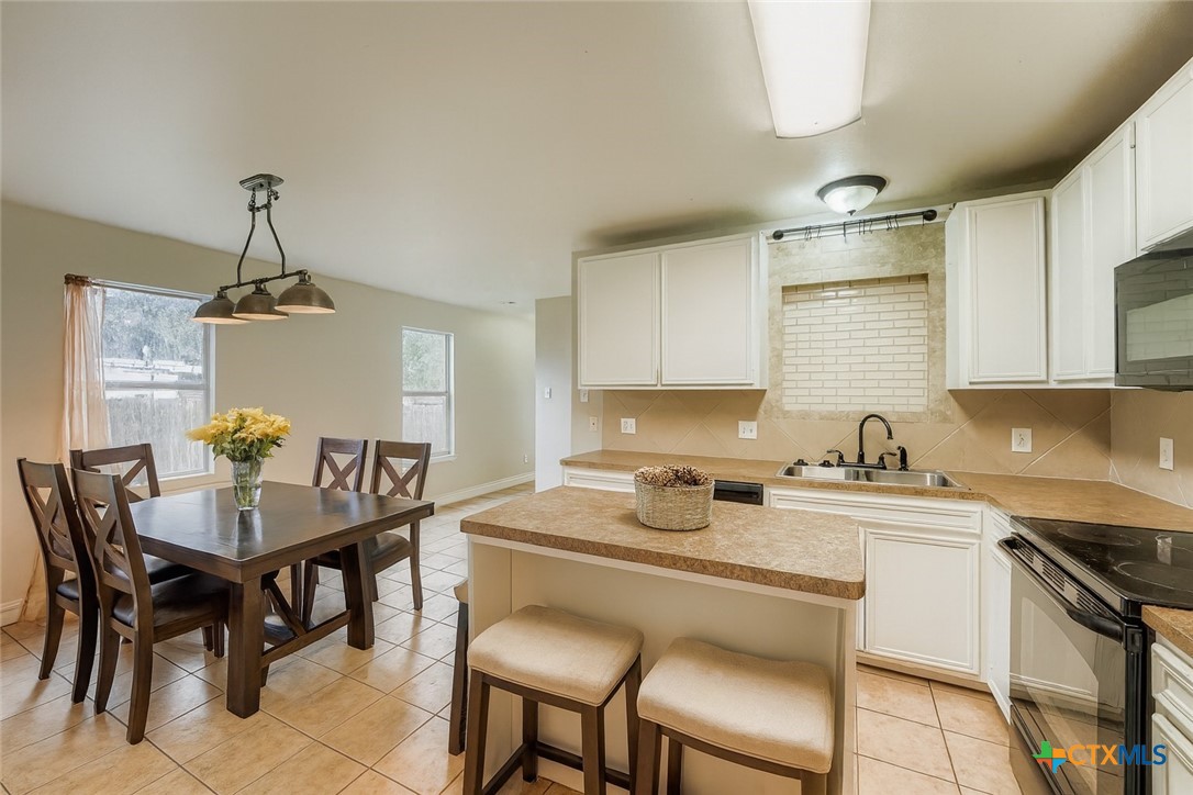 304 South Main Street Elgin, TX 78621 - Photo 4 of 25 Virtually staged -Kitchen featuring black appliances, white cabinets, decorative light fixtures, a center island, and backsplash