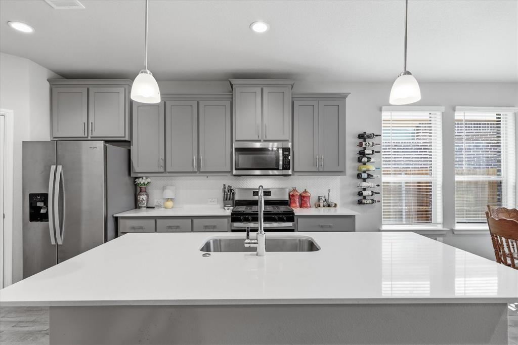 141 Medina Lane Rhome, TX 76078 - Photo 18 of 36 Kitchen featuring a large island with an undermount sink, pendant lighting, stainless steel appliances, and grey cabinetry