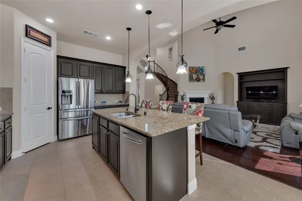 a kitchen with stainless steel appliances granite countertop a sink dishwasher a refrigerator and a fireplace with wooden floor