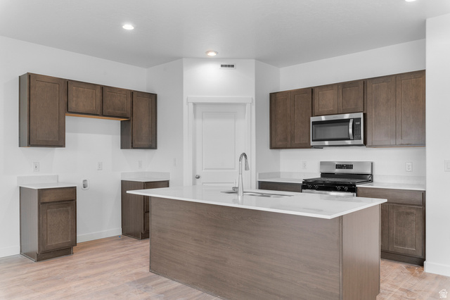 2829 South 710th West, Unit 17 Logan, UT 84321 - Photo 11 of 22 Kitchen featuring stainless steel appliances, a center island with sink, light wood-style flooring, recessed lighting, and light stone counters