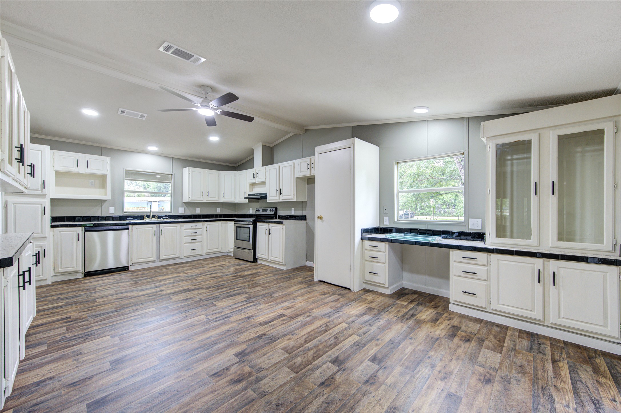 30226 Davis Street Magnolia, TX 77355 - Photo 4 of 50 This spacious kitchen features white cabinetry, stainless steel appliances, and dark countertops. It has ample natural light, a ceiling fan, and wood-style flooring, offering a modern and functional cooking space.