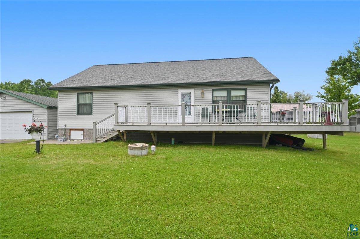8162 South Dowling Road West Superior, WI 54880 - Photo 14 of 15 Back exterior featuring a spacious deck with lattice railing, an attached garage with a white garage door, light-colored siding, and a dark-toned roof