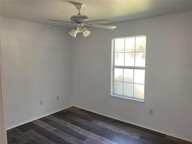 an empty room with wooden floor chandelier fan and windows