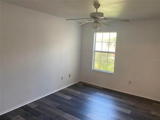 an empty room with wooden floor fan and windows