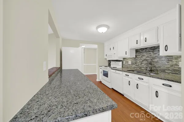 a large white kitchen with granite countertop a sink and white cabinets