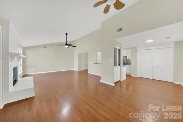a view of an empty room with wooden floor and a ceiling fan