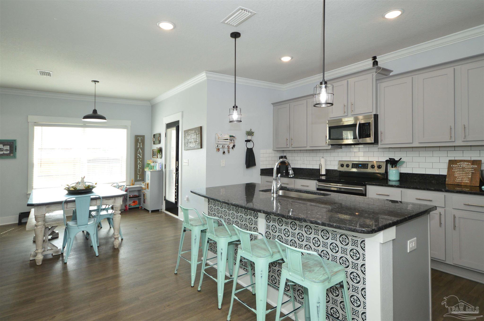 4453 Jude Way Pace, FL 32571 - Photo 17 of 41 a kitchen with stainless steel appliances granite countertop a stove a sink a microwave a dining table and chairs with wooden floor