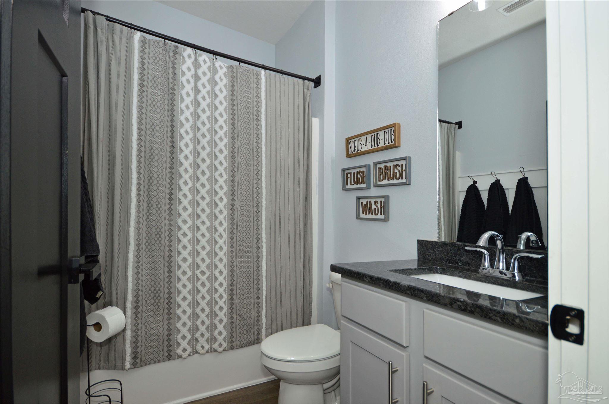 4453 Jude Way Pace, FL 32571 - Photo 25 of 41 a bathroom with a granite countertop sink a toilet and a shower curtain