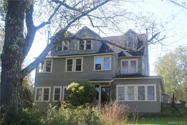 a view of a brick house with a yard plants and large tree