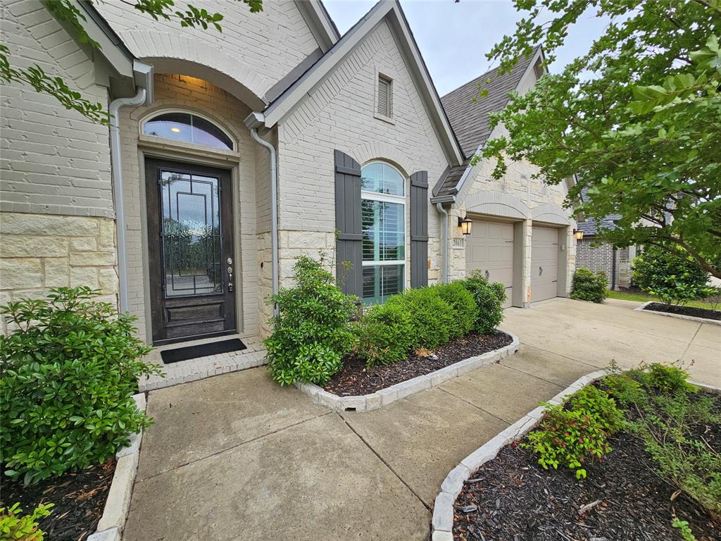 2065 Snapdragon Road Frisco, TX 75033 - Photo 3 of 39 Stone and brick facade featuring an arched entry with a decorative glass front door, flanked by a double garage with outdoor sconces