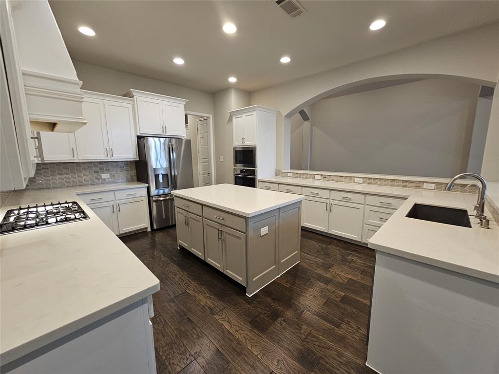 2065 Snapdragon Road Frisco, TX 75033 - Photo 4 of 39 Spacious kitchen featuring an expansive central island, stainless steel appliances, abundant cabinetry, stone countertops, and wood-finish flooring