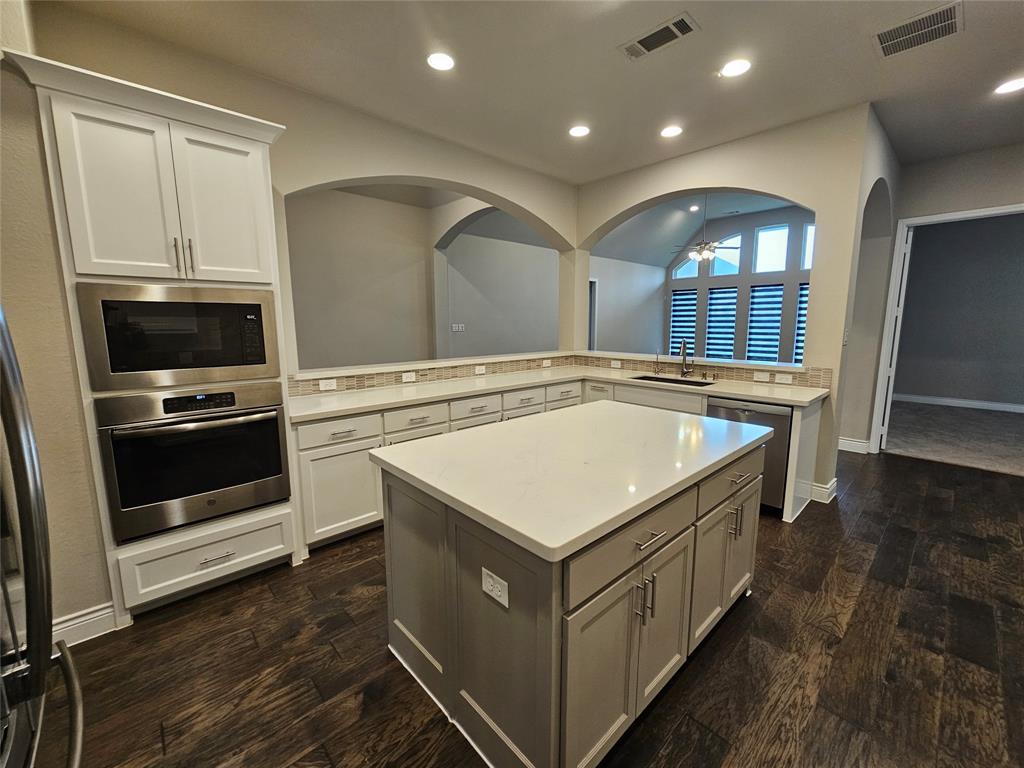 2065 Snapdragon Road Frisco, TX 75033 - Photo 7 of 39 Kitchen featuring an expansive center island with light-toned countertop, built-in stainless steel appliances, dark wood-finish flooring, and white and gray cabinetry