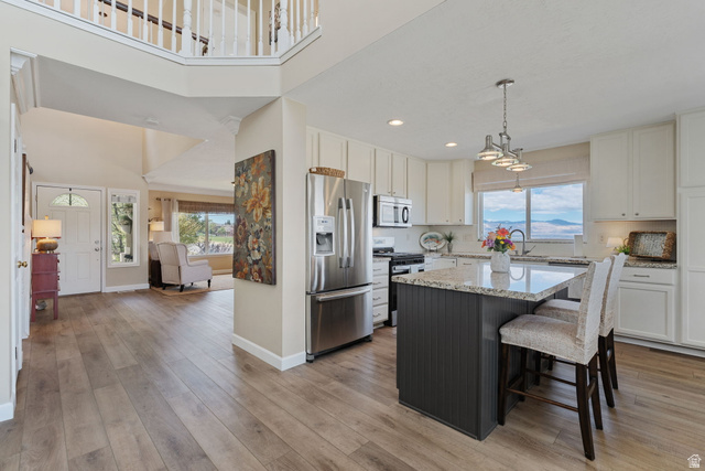 14883 Tooele Lane Draper, UT 84020 - Photo 19 of 49 Open-concept kitchen featuring an island with counter seating, stainless steel appliances, light-toned cabinetry, and wood-finish flooring