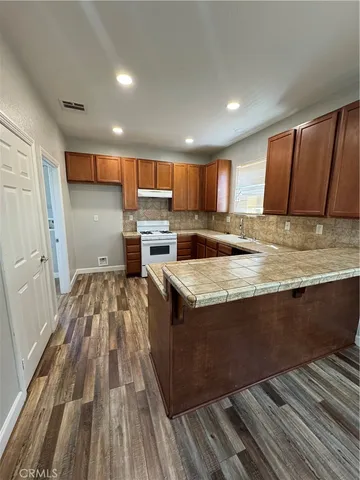 a kitchen with kitchen island granite countertop wooden floors a stove and a sink