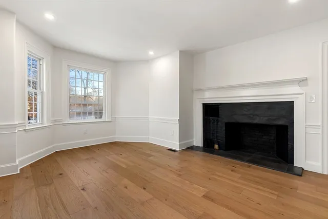 a view of an empty room with wooden floor fireplace and a window