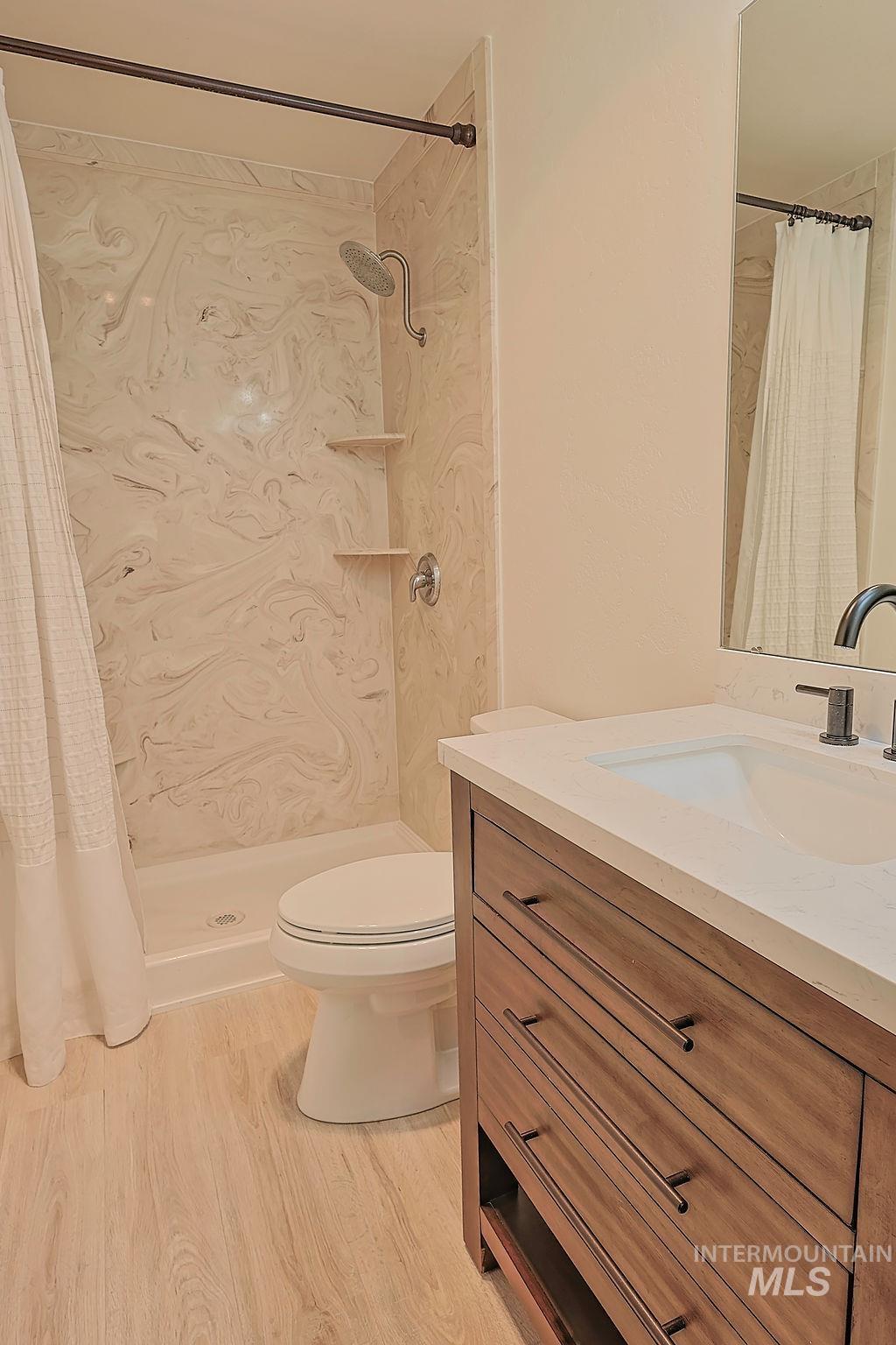 640 Morrison Street Twin Falls, ID 83301 - Photo 25 of 30 Full bathroom featuring a walk-in shower with decorative wall panels and built-in shelving, a single vanity with a white countertop and integrated sink, and wood-finish flooring