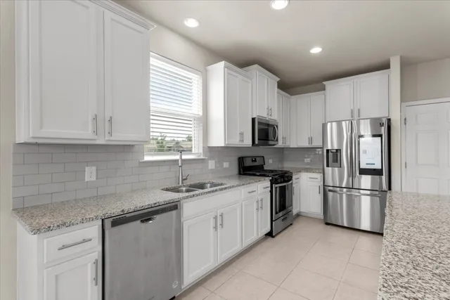 a kitchen with granite countertop a refrigerator a sink a stove a microwave a counter top space and cabinets