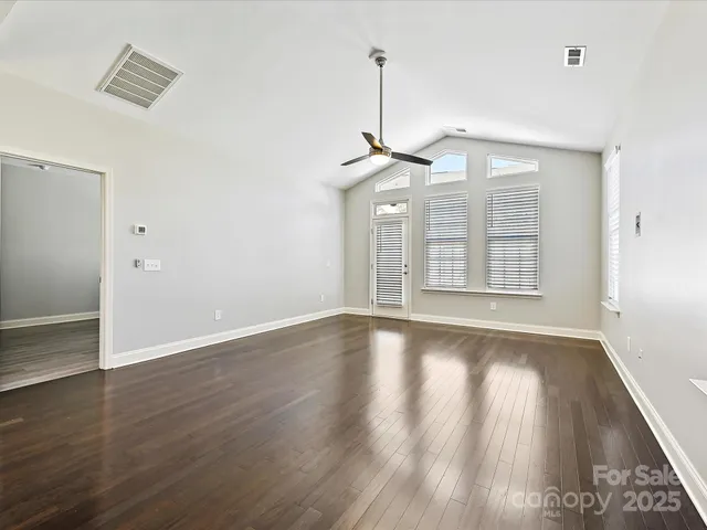 an empty room with wooden floor chandelier and windows