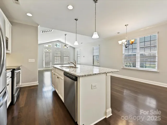 a kitchen with stainless steel appliances granite countertop a stove a sink a refrigerator and a wooden floor