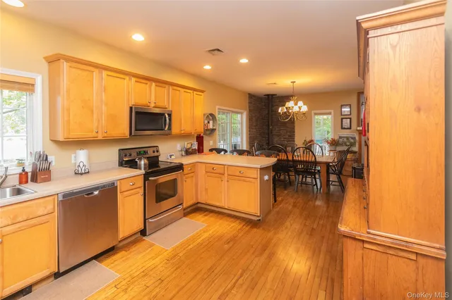 a kitchen with stainless steel appliances kitchen island granite countertop a stove top oven a sink a dining table and chairs with wooden floor