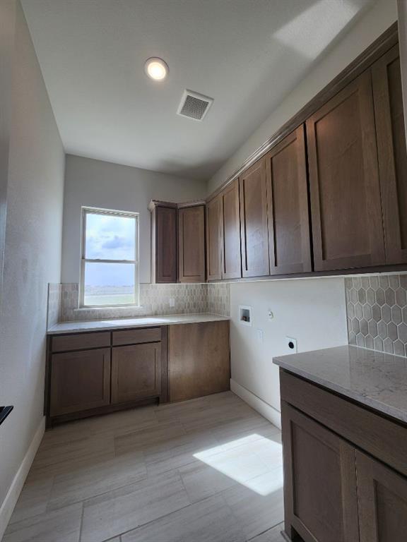 2305 Gypsum Street Krum, TX 76249 - Photo 17 of 22 Spacious utility room featuring extensive wood-finish cabinetry, light-toned countertops, and a full-height hexagonal tile backsplash