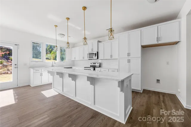 a kitchen with stainless steel appliances granite countertop a sink a stove a refrigerator and white cabinets with wooden floor