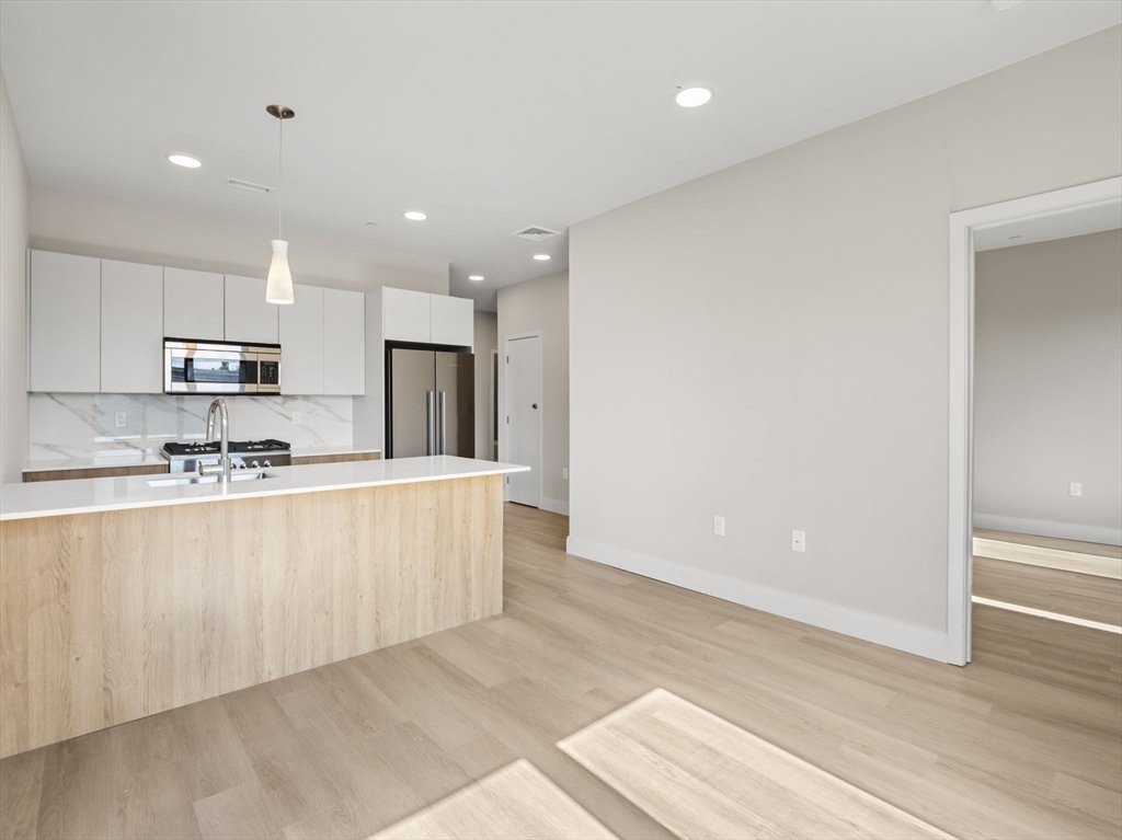 249 Corey Road, Unit 401 Boston, MA 02135 - Photo 8 of 34 a large kitchen with kitchen island a sink a stove a refrigerator and white cabinets with wooden floor