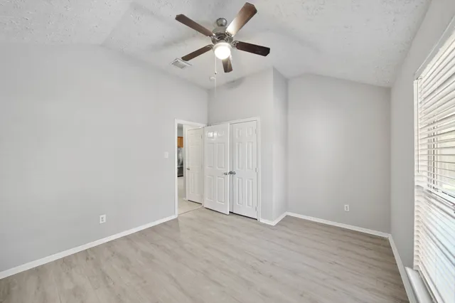 an empty room with wooden floor fan and windows