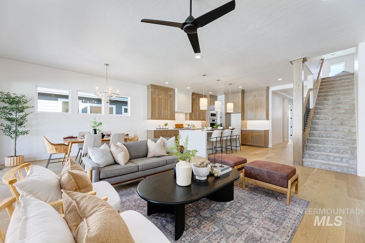 5817 South Gustav Avenue Meridian, ID 83642 - Photo 5 of 33 Open-concept living area featuring light wood-finish flooring, a modern black ceiling fan, and a prominent staircase with dark metal balusters