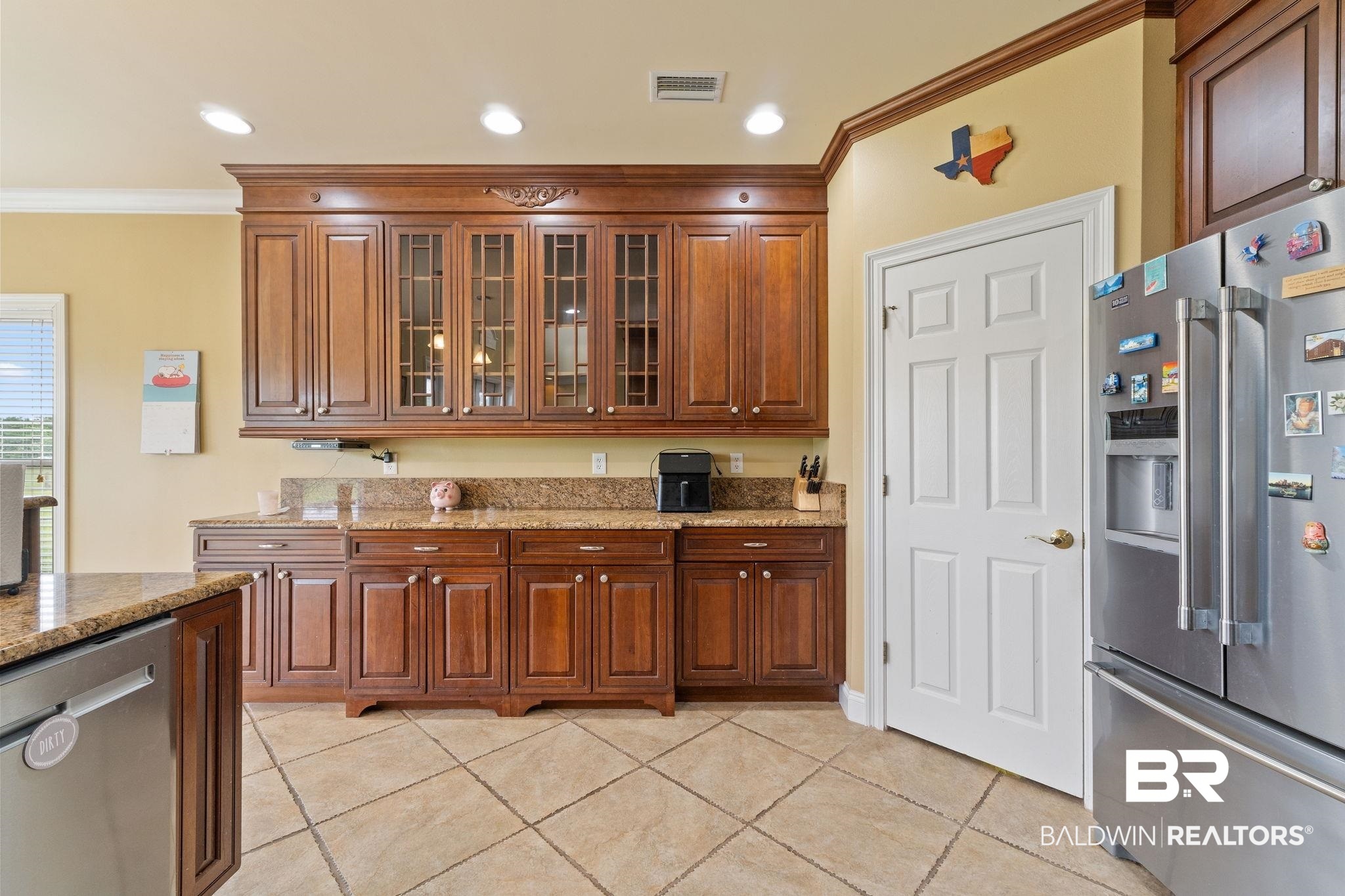 9790 Stucki Road Elberta, AL 36530 - Photo 34 of 72 Kitchen featuring appliances with stainless steel finishes, crown molding, light stone counters, glass insert cabinets, and light tile patterned flooring