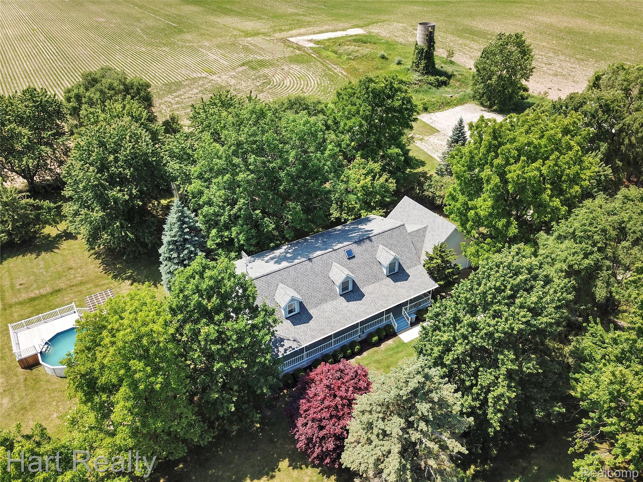 7167 Brown School Road North Branch, MI 48461 - Photo 2 of 51 Expansive property featuring a residence with a gray shingle roof and dormer windows, surrounded by mature trees, a manicured lawn, and an above-ground pool with an attached deck
