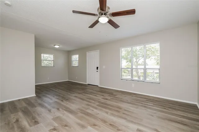 a view of an empty room with window ceiling fan and wooden floor